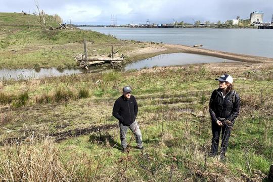 Two people stand on a grassy hill near a river