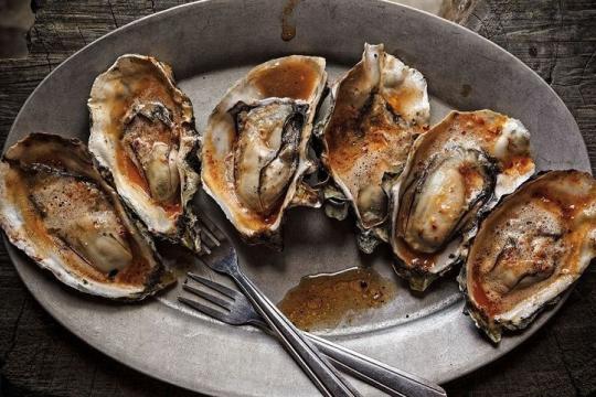 Six grilled Hog Island oysters drizzled in barbecue chipotle butter, on a serving dish with two small forks.